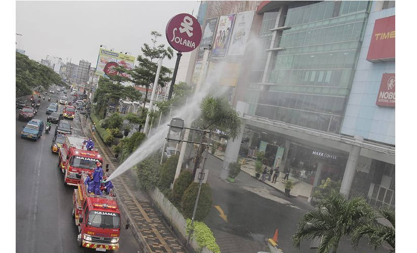 Petugas pemadam kebakaran menyemprotkan cairan disinfektan di jalan Margonda Raya
